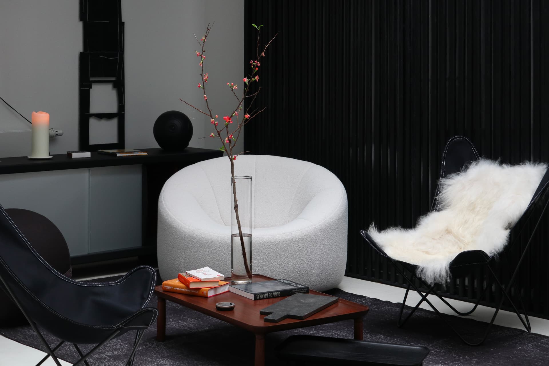 Salon minimaliste en noir et blanc : fauteuil bouclé clair, branche fleurie dans un vase et table basse en bois